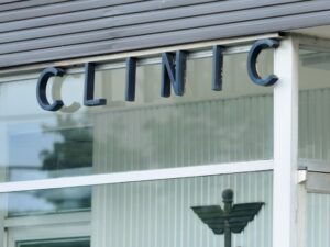 Local Clinics Close-up view of a ‘Clinic’ sign on a modern glass building exterior.