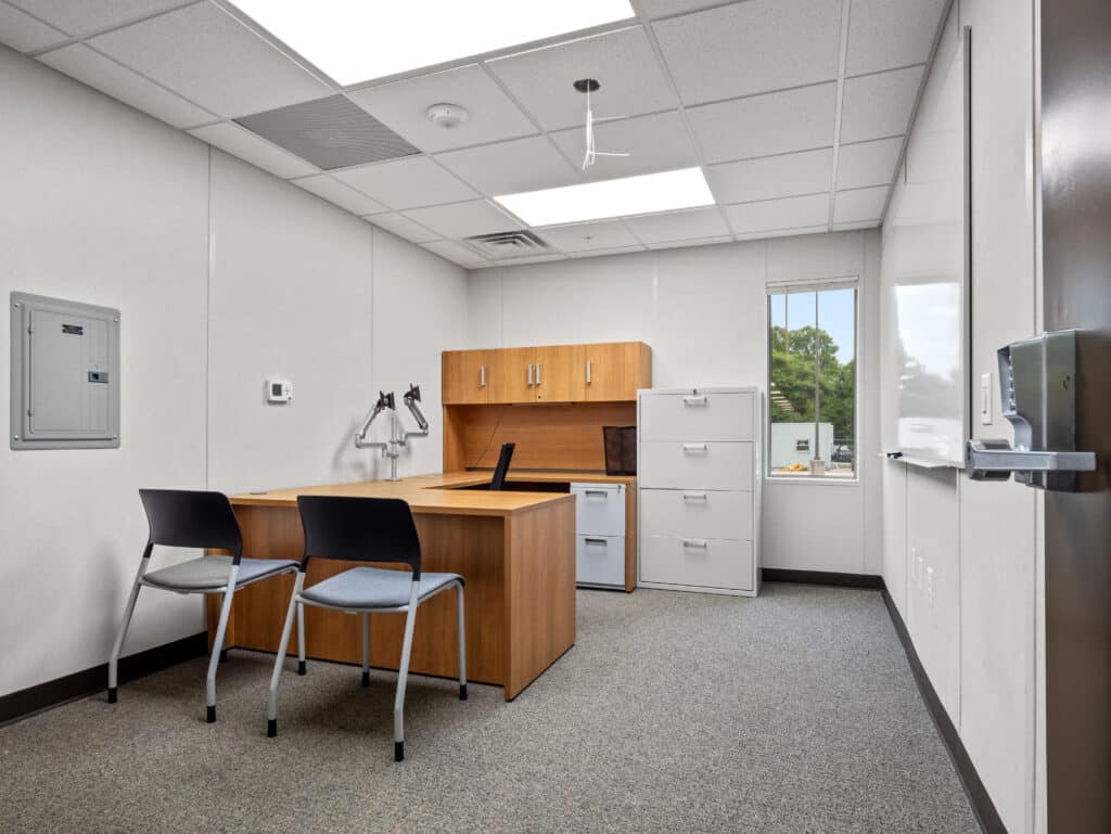 Private office furnished with desk, storage, monitor arms and guest chairs in the modular office building