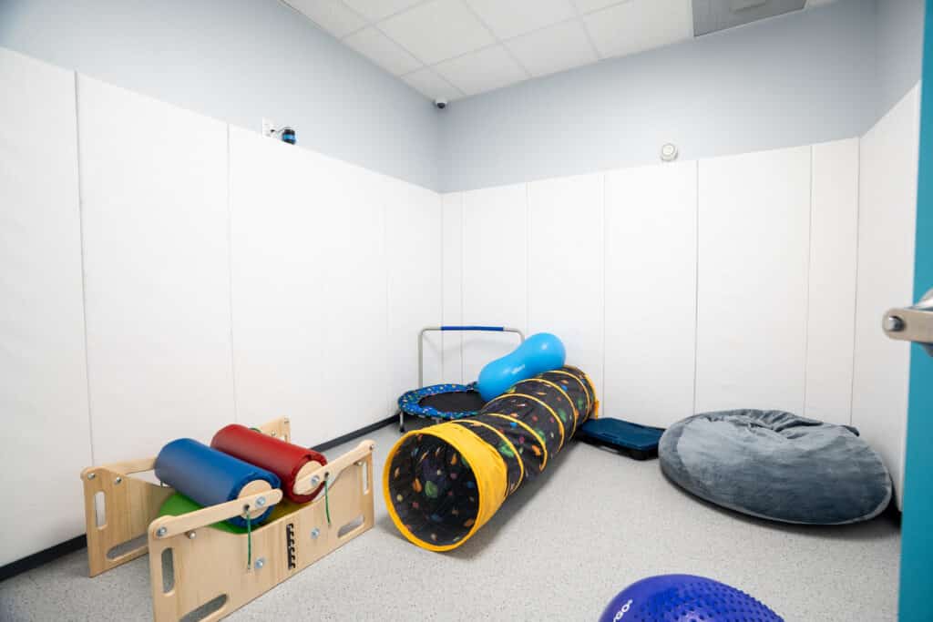 Padded sensory motor room with a crawl tunnel, therapy rolls, a mini trampoline and a bean bag